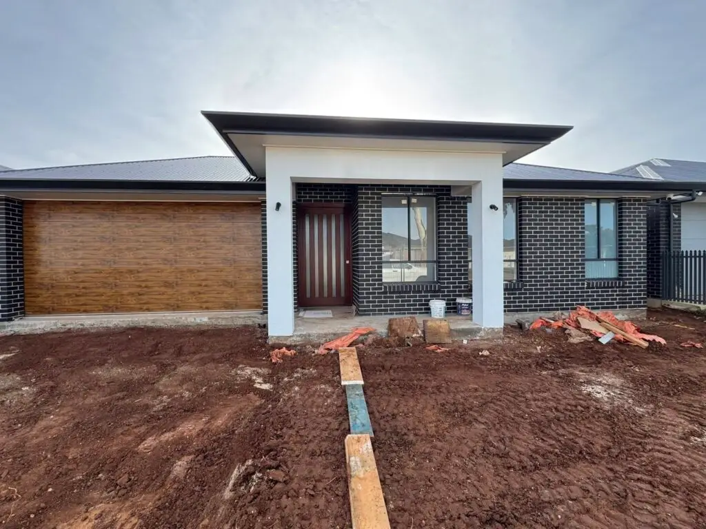 Modern single-storey home under construction with dark brick exterior and timber garage door