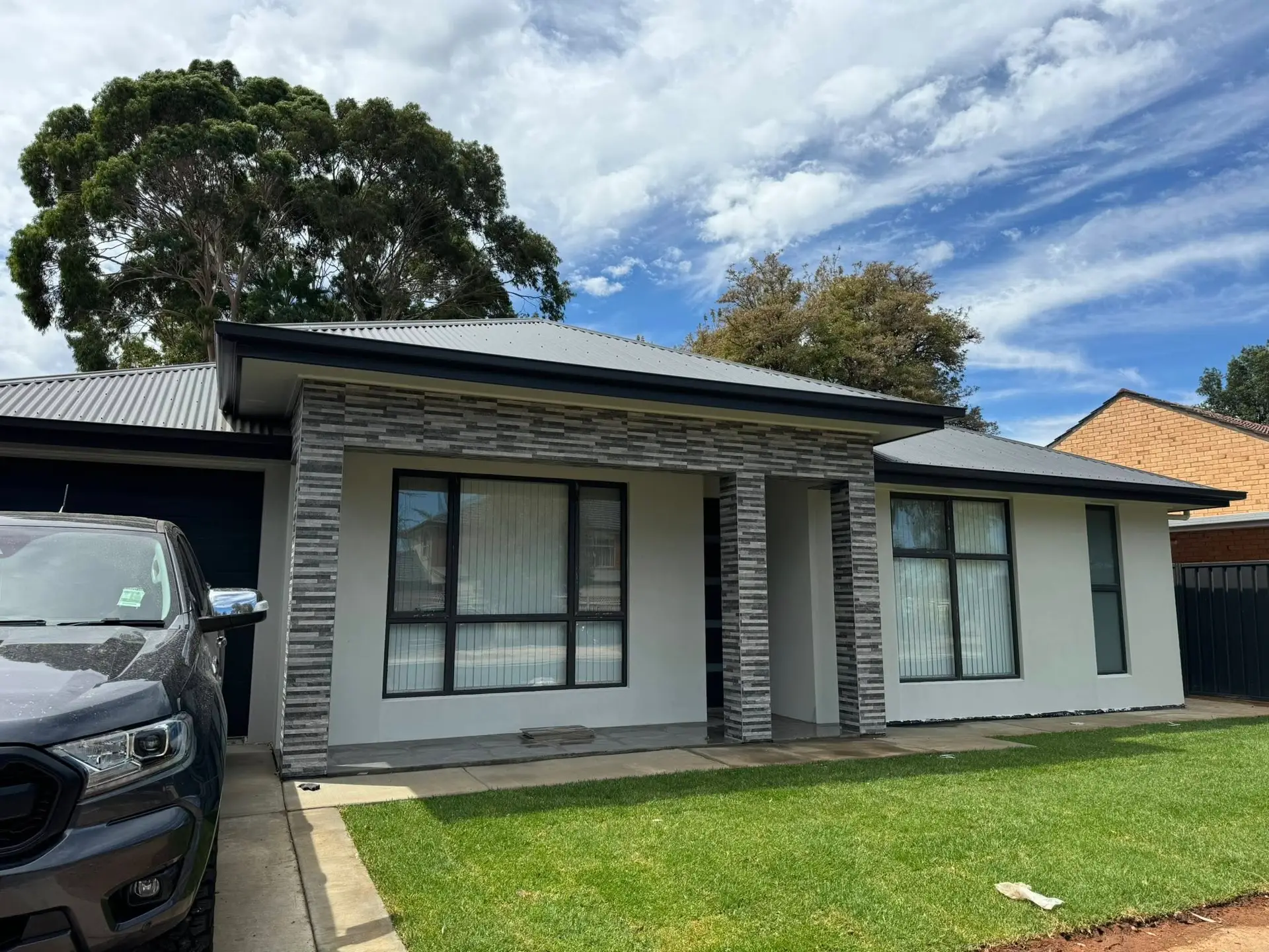 Modern single-storey home with grey brick columns, rendered walls, and metal roof